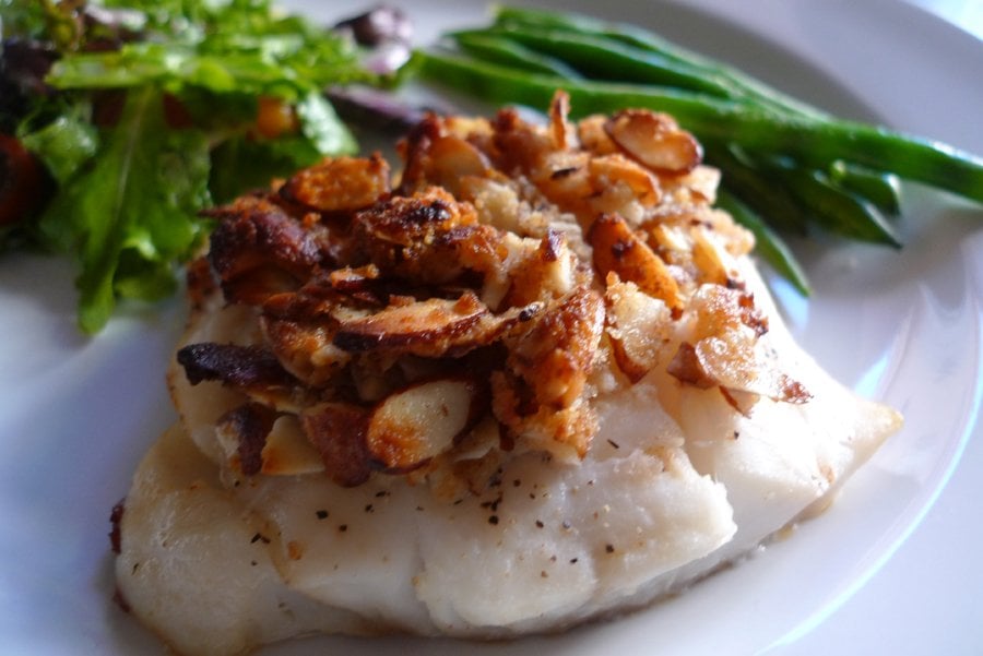 Almond Crusted Cod showing a cod filet topped with an almond-panko blend. Green beans and salad shown in background.