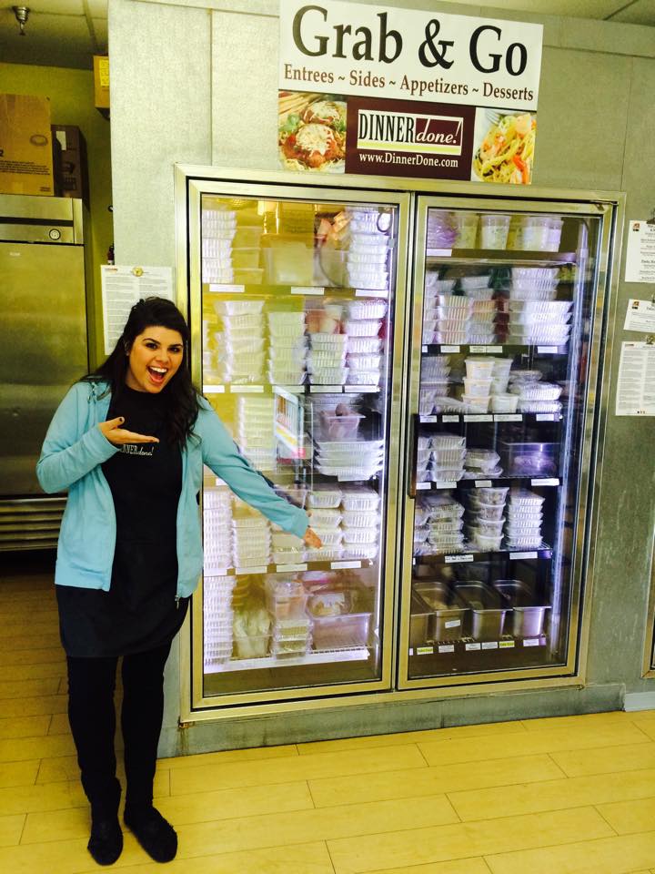 A customer service team member showing Dinner Done's entrees arranged in a freezer with glass doors.