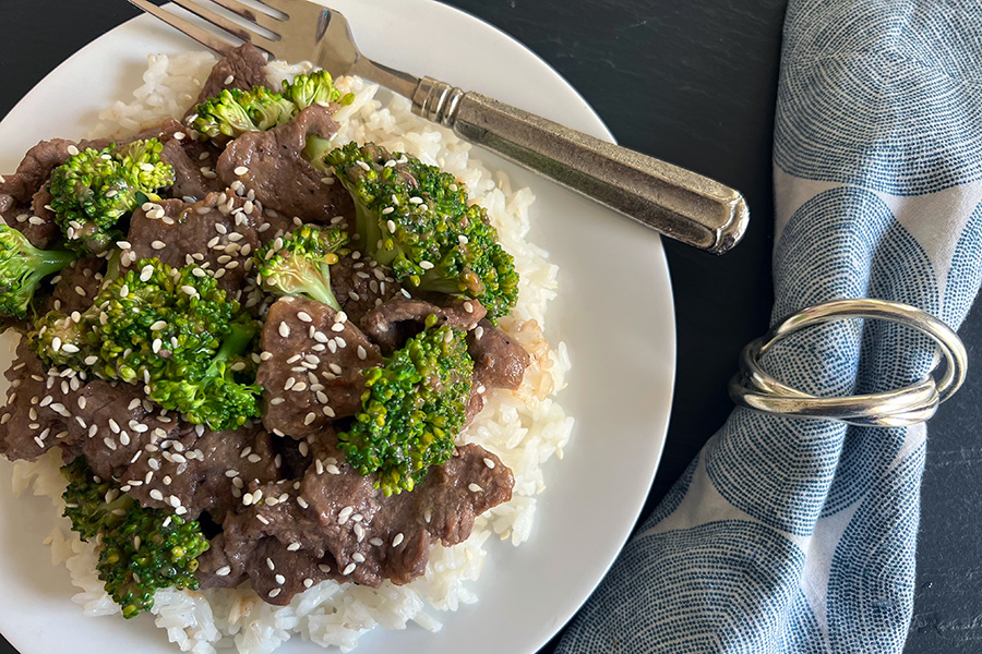 Beef & Broccoli Stir Fry over Rice sprinkled with sesame seeds, shown with a decorative napkin.