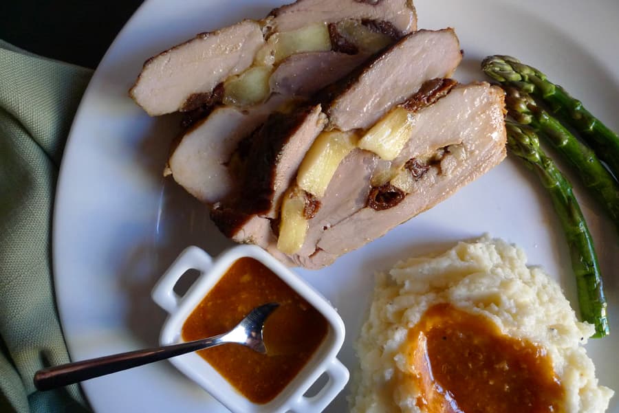 Apple and raisin stuffed pork sliced with side of cider gravy, shown with mashed potatoes and asparagus.