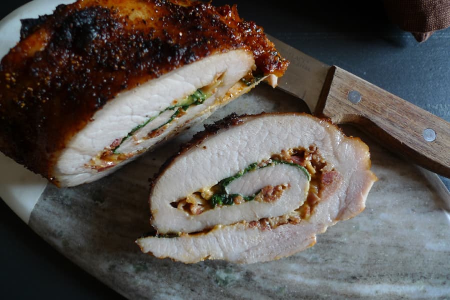 A pork loin filled with bacon, cheddar, and spinach sliced. Shown with a knife.