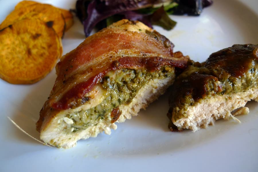 Bacon Topped Chicken breast filled with mozzarella cheese and pesto, sliced. Shown with sliced sweet potatoes and salad.