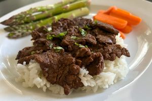 Balsamic glazed beef tips over parmesan rice, shown with carrots and asparagus.