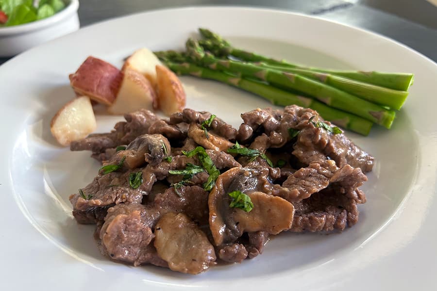 Beef slices in Diane sauce with mushrooms, shown with baby potatoes and asparagus.