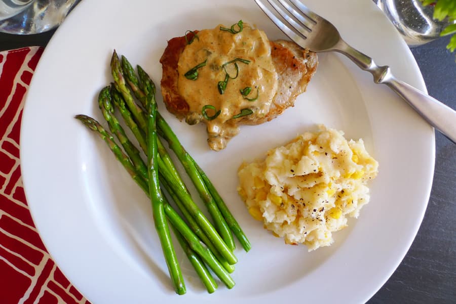 Pork Chops with Basil Cream Sauce shown served with mashed potatoes and asparagus.