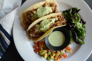 Pork Tacos with Creamy Cilantro Sauce shown served with diced vegetables and salad.