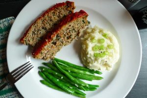 Quinoa Turkey Meatloaf, a turkey meatloaf with quinoa and spinach, is shown served with mashed potatoes and green beans.