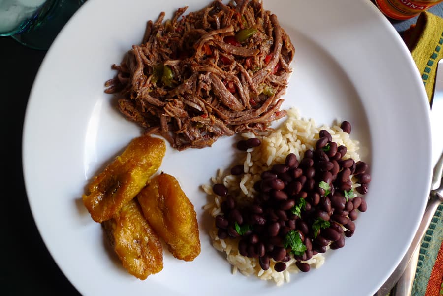 Ropa Vieja with Black Beans and Rice shown served with a side of plantains.