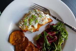 Twisted Teriyaki Chicken, a teriyaki marinated chicken breast topped with cheddar, cheese, bacon, and our ranch-style sauce, shown served with salad and sweet potato slices.