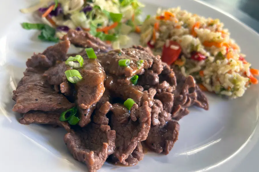 Beef Tips in Robert Sauce with Veggie Pilaf, served with a salad and garnished with sliced green onions.