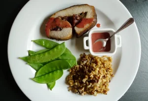 A slilce of Cranberry Walnut Stuffed Pork Roast plated with sauce, shown with snow peas and rice as side dishes.