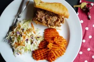 Carolina Pulled Pork served in a sliced baguette with side dishes.