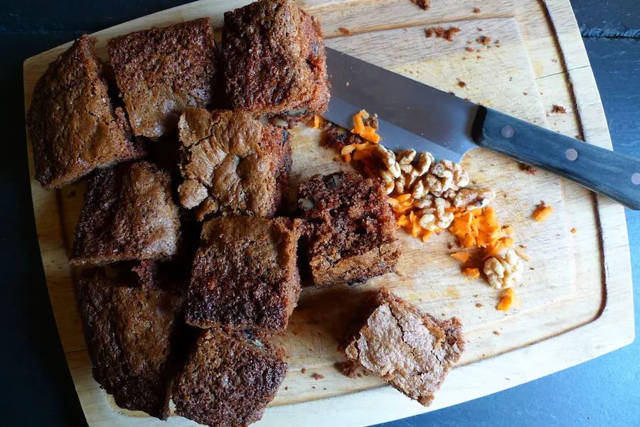 Carrot cake cut into squares on a cutting board.