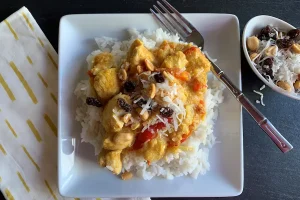 Chicken Curry over Rice shown with side bowl of peanut, coconut, and raisin toppers.