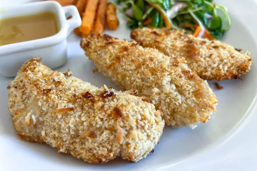 Close up of Coconut Chicken Fingers with Orange Sauce shown plated with sides.