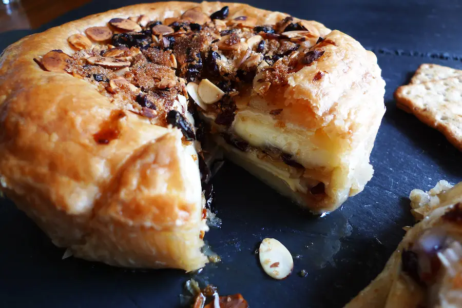 A one pound round of Cranberry Almond Baked Brie shown wiht a slice taken out so you can see filling in the middle.