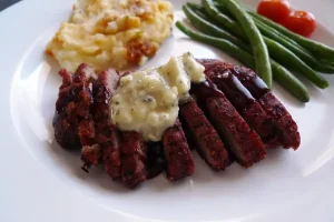 Flank Steak with Rosemary Gorgonzola Butter and Red Wine Sauce shown plated with side dishes.