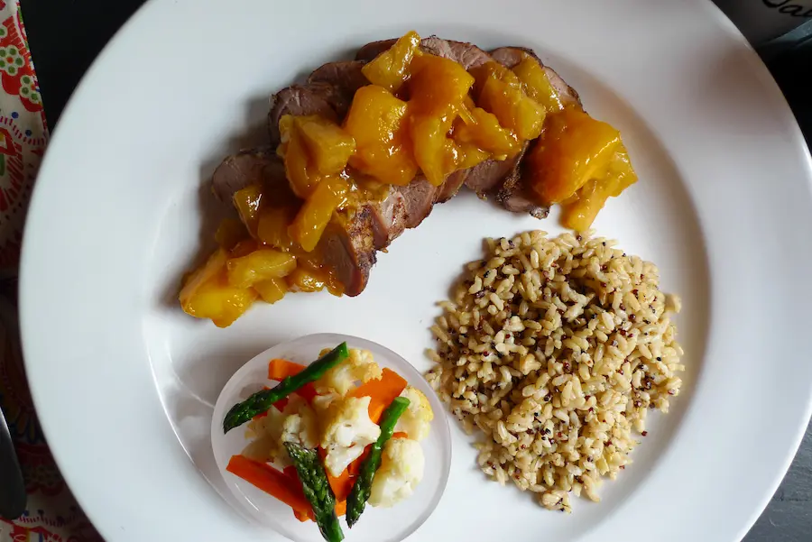 Jamaican Pork Tenderloin with Island Chutney shown sliced and plated with side dishes.