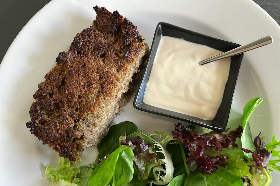Mediterranean Meatloaf shown with the garlic yogurt sauce, and a side of salad.