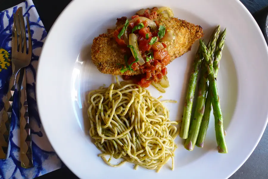 Parmesan Pesto Chicken with Bruschetta shown plated with pasta and asparagus.