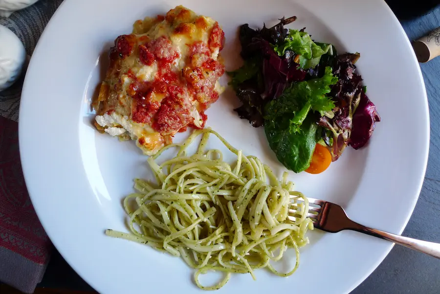Pesto Bruschetta Chicken shown plated with suggested sides of pasta and salad.